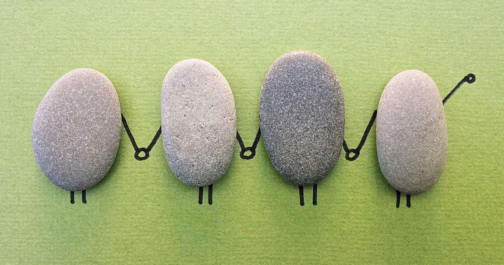 Rocks placed in a line, on a green background with hands drawn on them